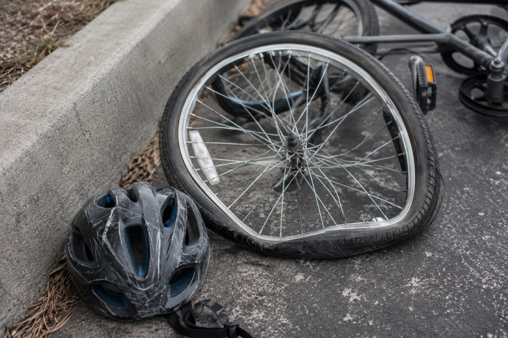 Damaged bicycle with a bent, detached front wheel and scratched helmet lying beside a curb, conveying a somber roadside accident scene.